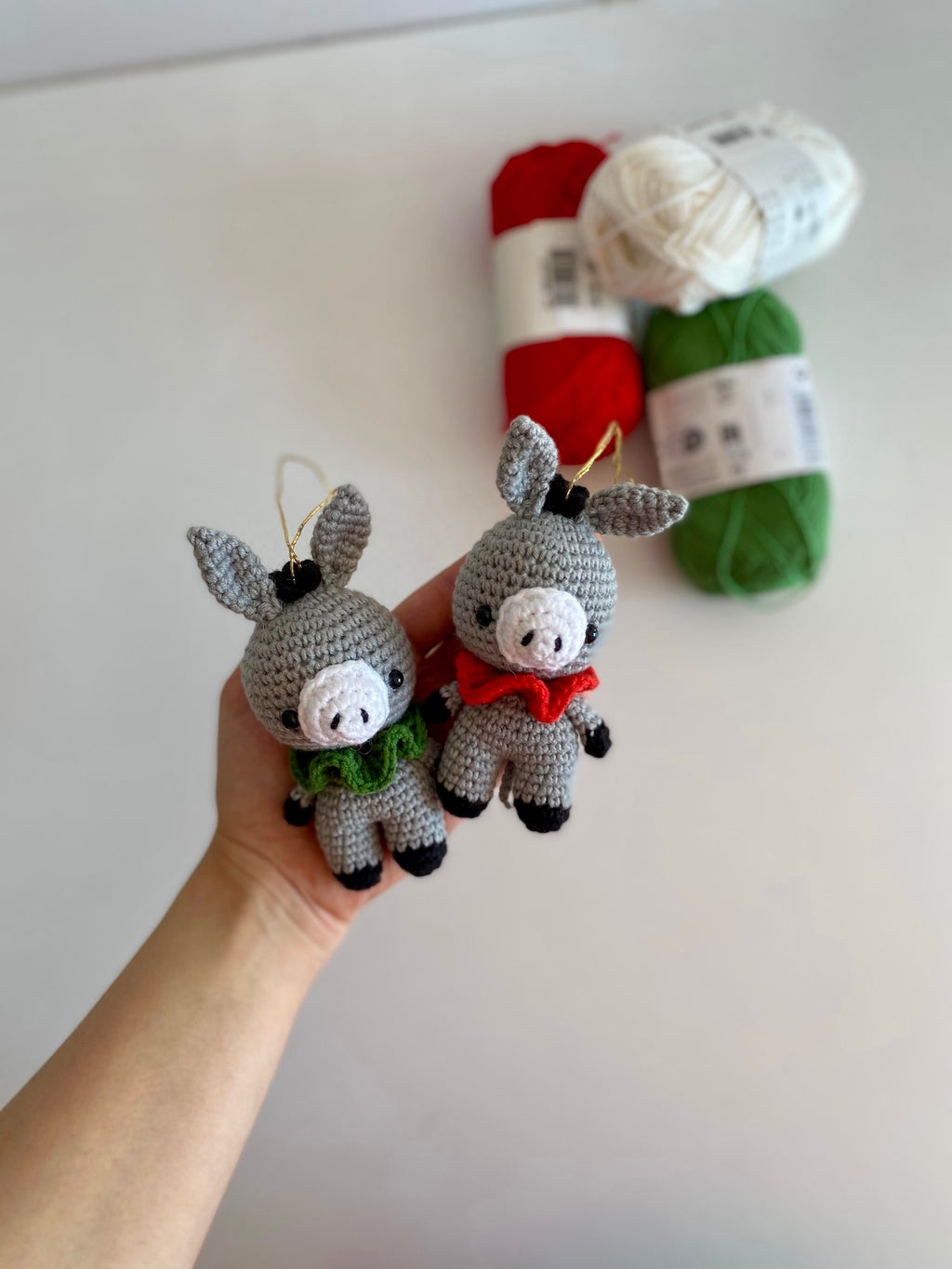 Two small crochet donkey toys held in a hand with yarn balls in the background.